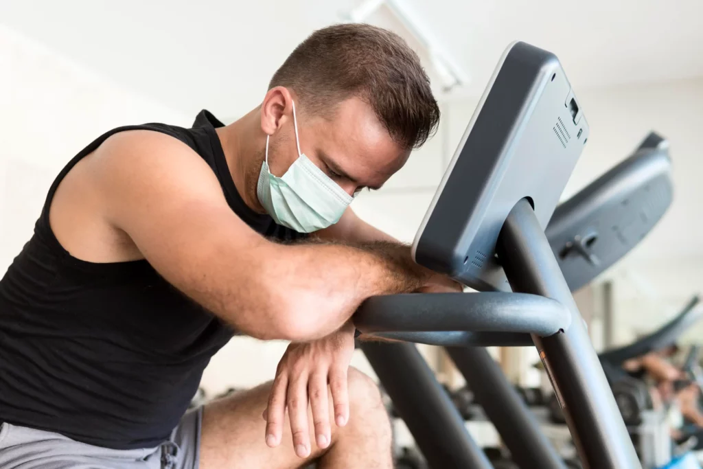 Homme fatigue faisant du cardio en salle de sport avec masque illustrant la question peut on faire du sport en etant malade