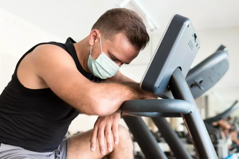 Homme fatigue faisant du cardio en salle de sport avec masque illustrant la question peut on faire du sport en etant malade