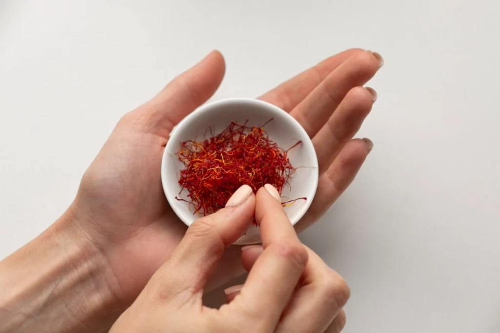 Main tenant une cuillère de safran en poudre, safran en complément alimentaire, étudié pour le soutien de l'humeur pendant la ménopause