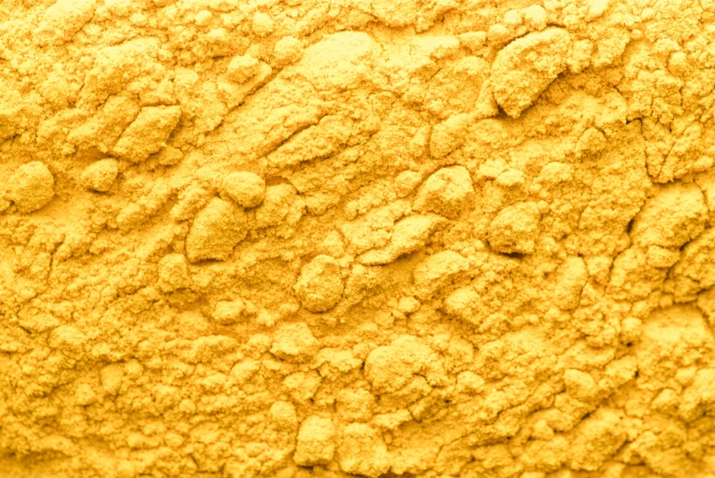 Gros plan texture poudre de maca jaune, ingrédient naturel sujet de plusieurs essais cliniques sur le bien-être féminin à la ménopause
