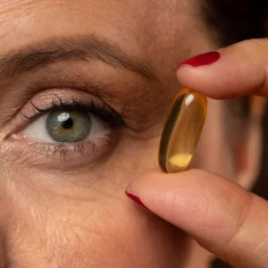 Gros plan sur le visage d'une femme mature tenant entre ses doigts une capsule de complément alimentaire, illustrant le guide comparatif pour choisir les meilleurs compléments alimentaires à la ménopause
